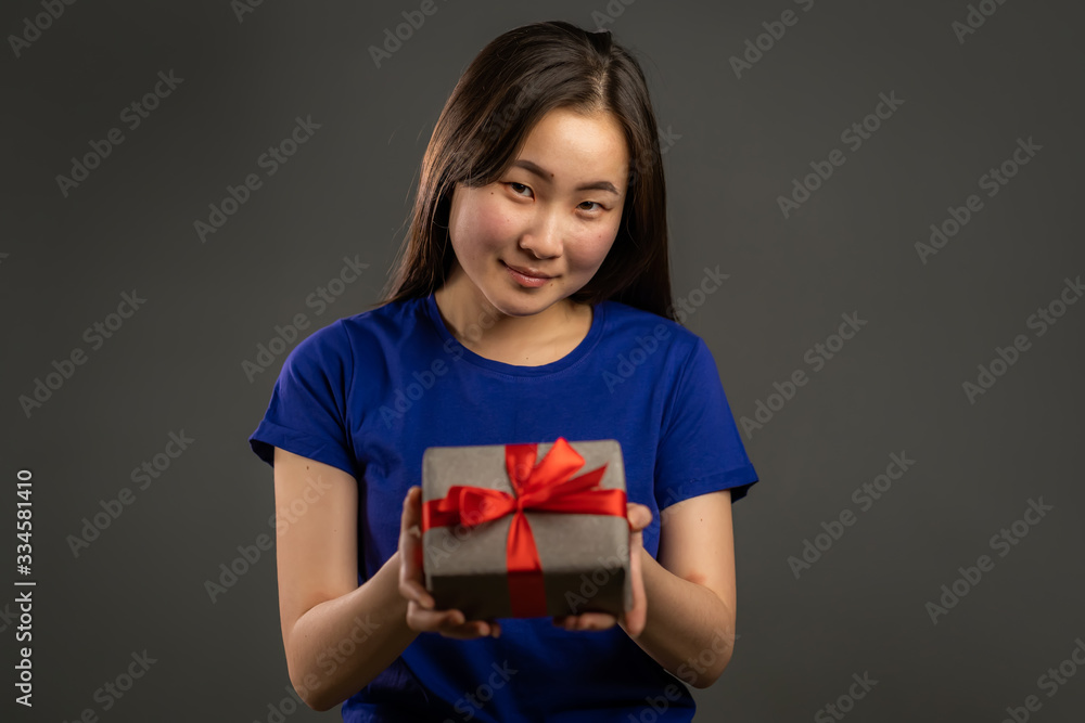 Excited asian girl gives gift and hands it to the camera. She is happy. Korean girl on grey background. Studio portrait Excited asian girl gives gift and hands it to the camera. She is happy. Korean girl on grey background. Studio portrait