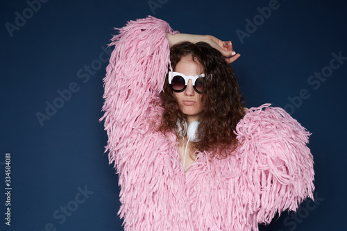 Attractive lady moves body actively, raises hands, has fun during party, feels rhythm of music, dressed in stylish authentic clothes,pouring lips, isolated indoors, picks favorite song for good mood.