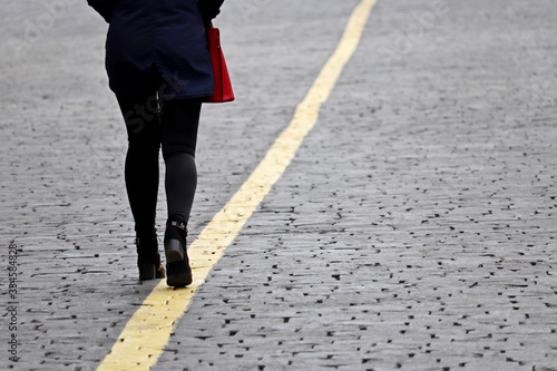Slim girl in spring clothes walking on the yellow line on a street, rear view. Concept of ladies fashion, following a goal, career and life's ambition