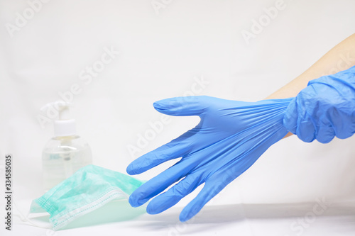 A person putting on some gloves next to anti bacterial hand gel and a surgical face mask