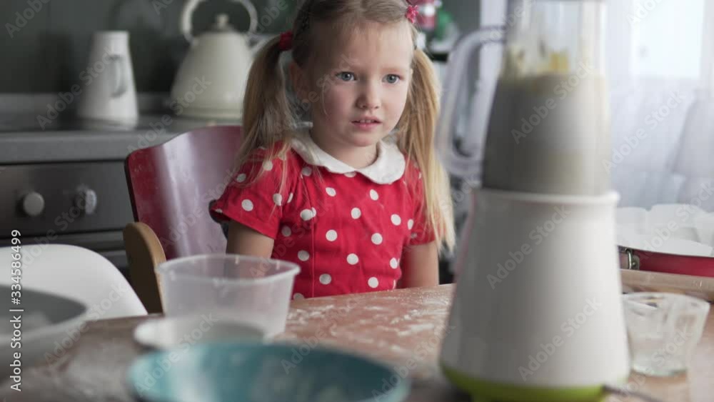 The little girl turns on the blender at home in the kitchen. Child learn to cook cake at home The little girl turns on the blender at home in the kitchen. Child learn to cook cake at home