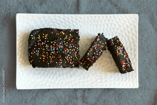 homemade Cocoa cake with chocolate flavored icing and colorful sprinkles, placed on a white porcelain tray