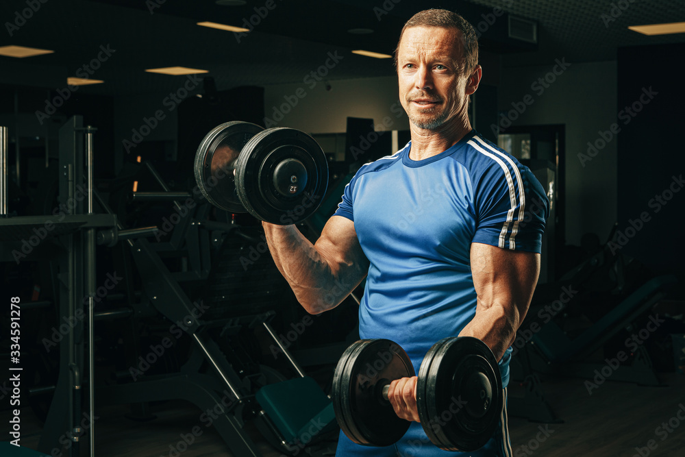 Senior man in his fifties lifting weights in a gym Senior man in his fifties lifting weights in a gym