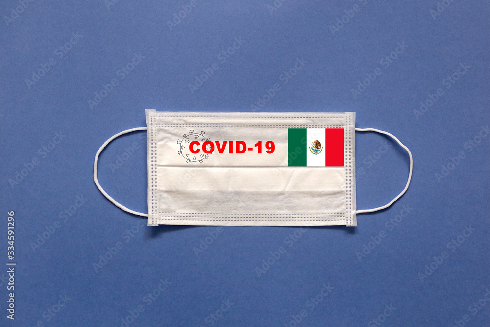 Mexico flag and inscription COVID-19 on a medical mask on a blue background. Healthcare and medical concept. Pandemic virus COVID-19