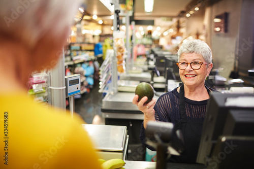 Smiling senior female cashier helping customer at grocery checkout photo