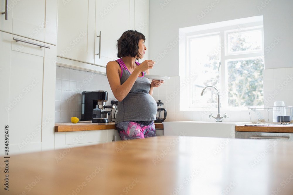 Thoughtful pregnant woman eating in kitchen looking out window Thoughtful pregnant woman eating in kitchen looking out window