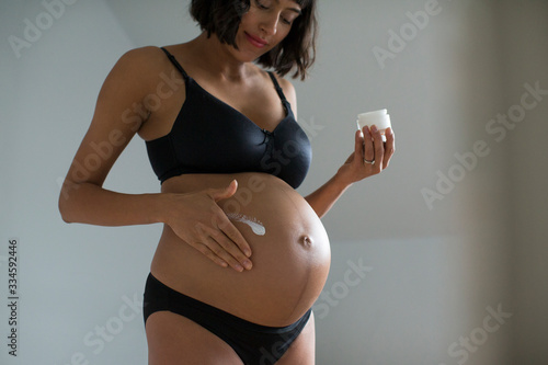 Pregnant woman in bra and panties applying moisturizer to stomach