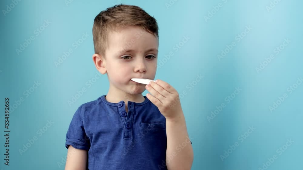 Ill young child with a thermomether, measuring the height of his fever and looking into the camera Ill young child with a thermomether, measuring the height of his fever and looking into the camera
