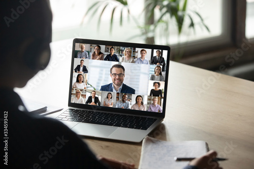 Back view of female employee engaged in team Webcam conference on laptop, have online briefing or consultation from home, woman worker speak talk on group video call with diverse colleagues photo