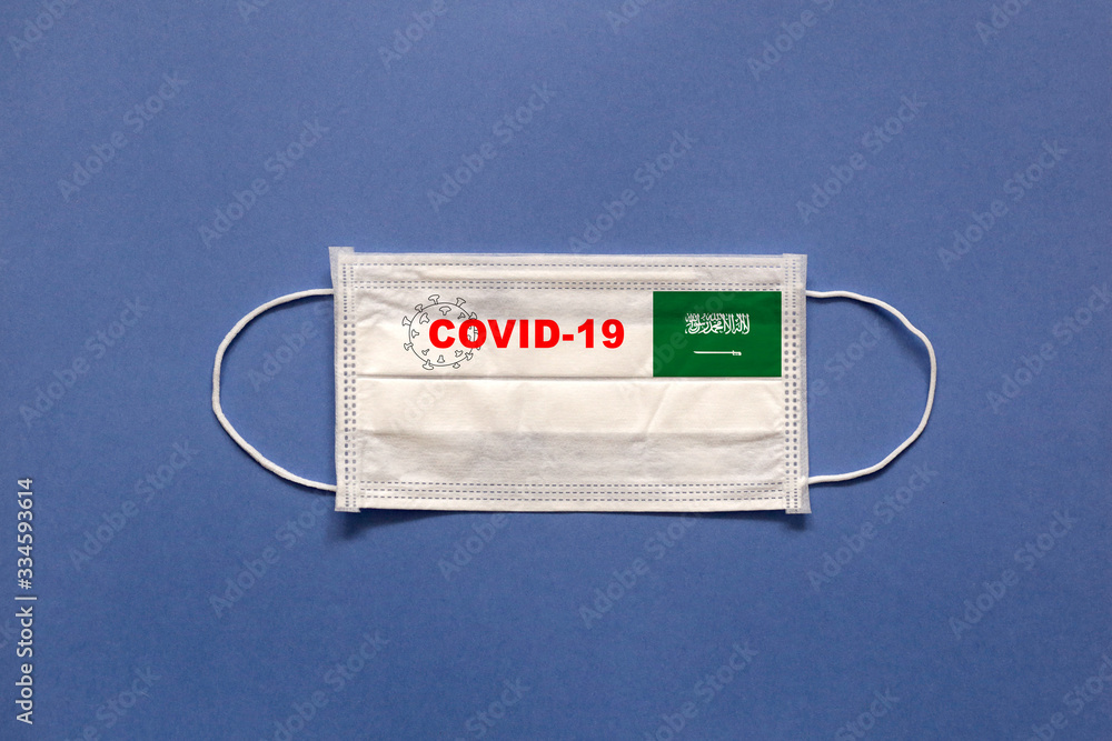 Flag of Saudi Arabia and inscription COVID-19 on a medical mask on a blue background. Healthcare and medical concept. Pandemic virus COVID-19 Flag of Saudi Arabia and inscription COVID-19 on a medical mask on a blue background. Healthcare and medical concept. Pandemic virus COVID-19