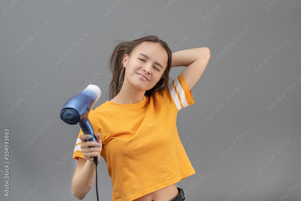 Beautiful hairstyle and scalp care. Girl dries hair with a hairdryer on a gray background, smiling Beautiful hairstyle and scalp care. Girl dries hair with a hairdryer on a gray background, smiling