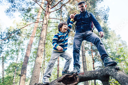 little son with father climbing on tree together in forest, lifestyle people concept, happy smiling family on summer vacations