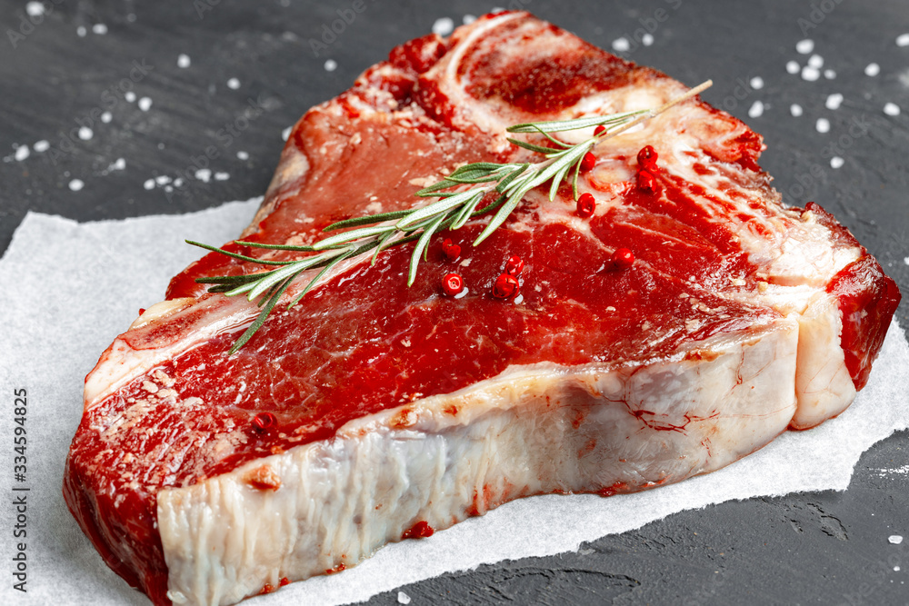Obraz premium Raw fresh meat t-bone steak with spices on a dark background, close up
