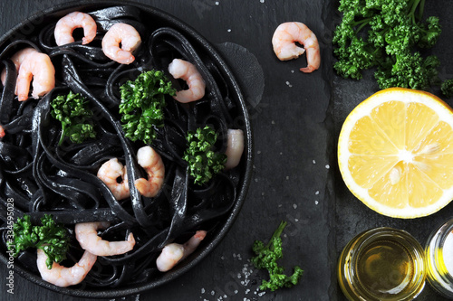 Black pasta with shrimp and parsley on a graphite black surface. Minimalistic black food. Black food concept.