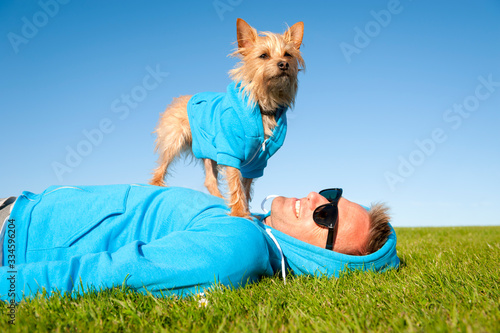 Man relaxing with best friend dog in matching blue hoody sweatshirts on bright green grass meadow