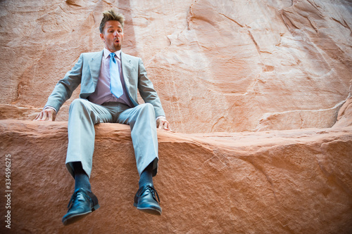 Obraz na plátně Nervous businessman sitting outdoors on the ledge of steep cliff face looking do