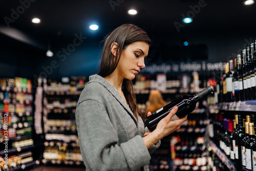 Woman shopping for expensive wine in supermarket alcohol store.Choosing and buying good cheap wine.Benefits of drinking wine.Resveratrol.Everyday binge drinking.Oenology.Mediterranean diet.Alcoholism
