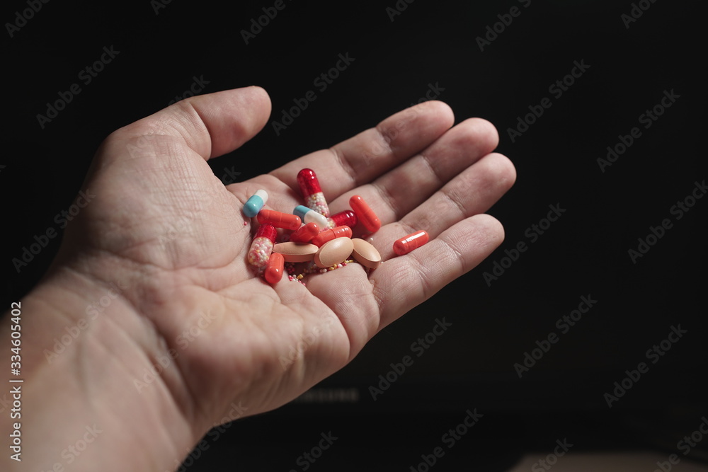 Close-up of a man's hand on a dark background, holding a variety of different tablets and pills. Close-up of a man's hand on a dark background, holding a variety of different tablets and pills.