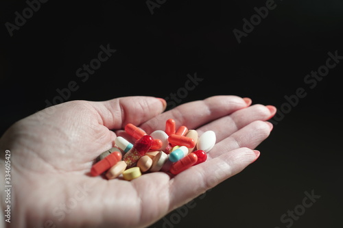 Close-up of a man's hand on a dark background, holding many different tablets in the palm.