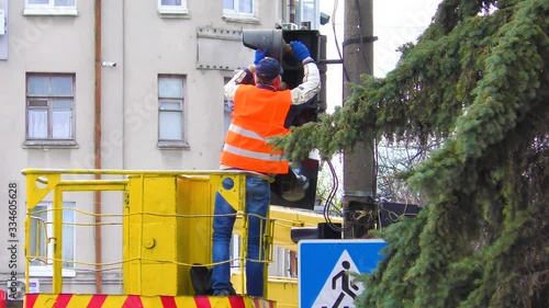 Electrical workers are busy repairing a broken traffic light on a busy intersection. Traffic light repairman worker