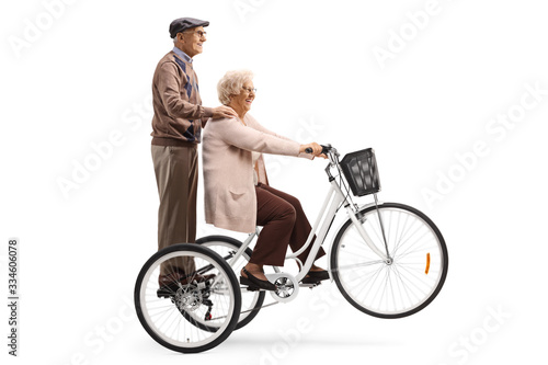 Senior woman riding a tricycle and a senior man behind her