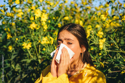 Allergy, medical, seasonal flowers concept. Allergy to flowering. Sneezing and runny nose from pollen. Amazing woman in the park holds a handkerchief and sneezes from the bloom of flowers and pollen.