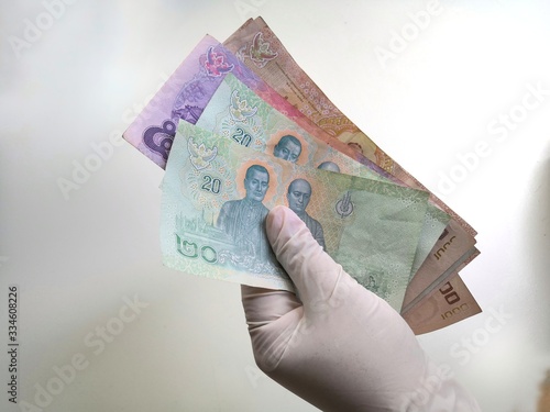 2020 in Thailand. The image of money grabbing by hand wearing rubber gloves to prevent contamination of the virus or the covid-19 