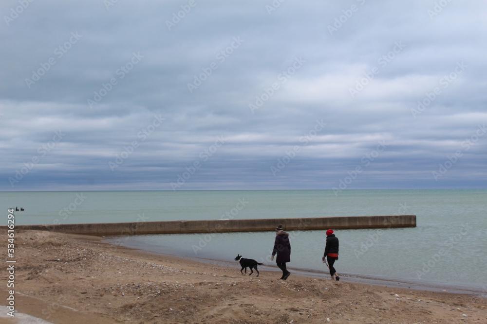 Two women walking a dog on the beach with a greenish Lake Michigan at Loyola Park in Chicago