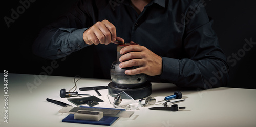 Jewelry craftsmanship, engraving. Jeweller engraver hands at work. Professional engraver tools for jewelleries manufacturing on white desk. Craftsman, engraver, goldsmith workplace 