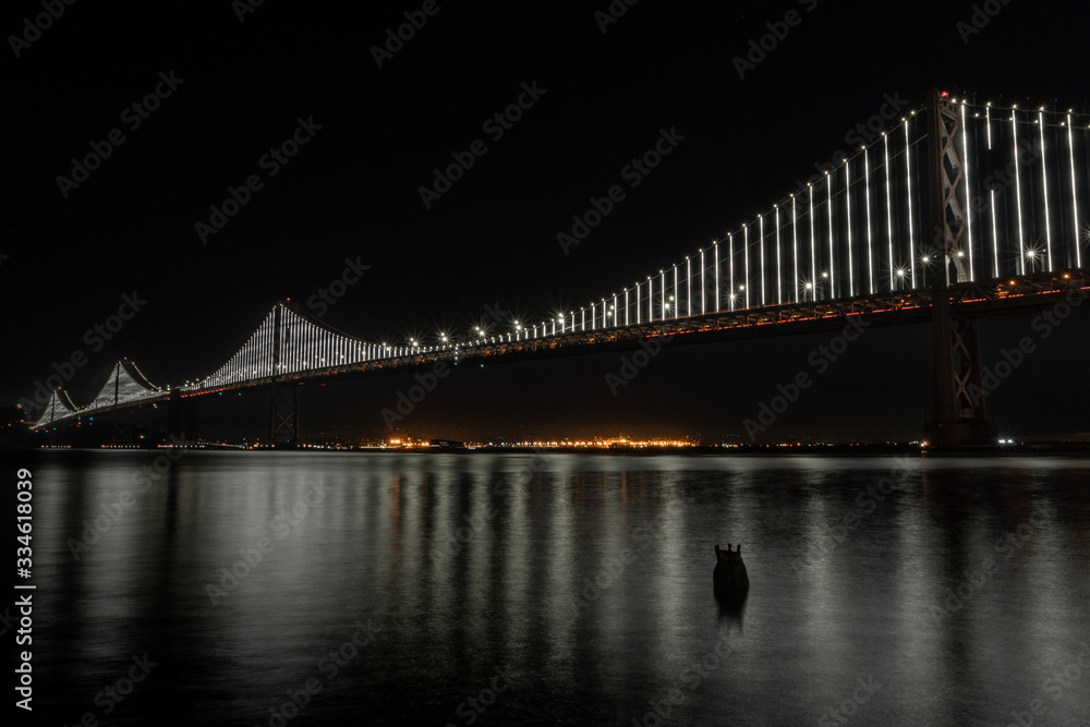 Natural San Francisco Bay Bridge with Oakland in background and water reflection night photo. Bay Area, California. 