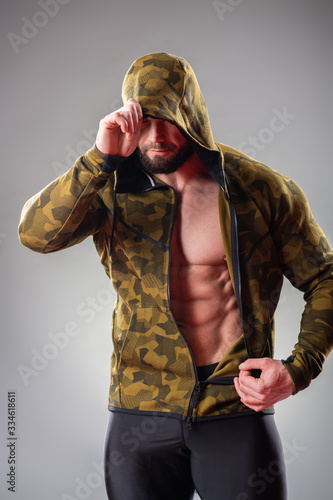 Sexy muscular bodybuider posing with sweatshirt and hood on the gray background photo