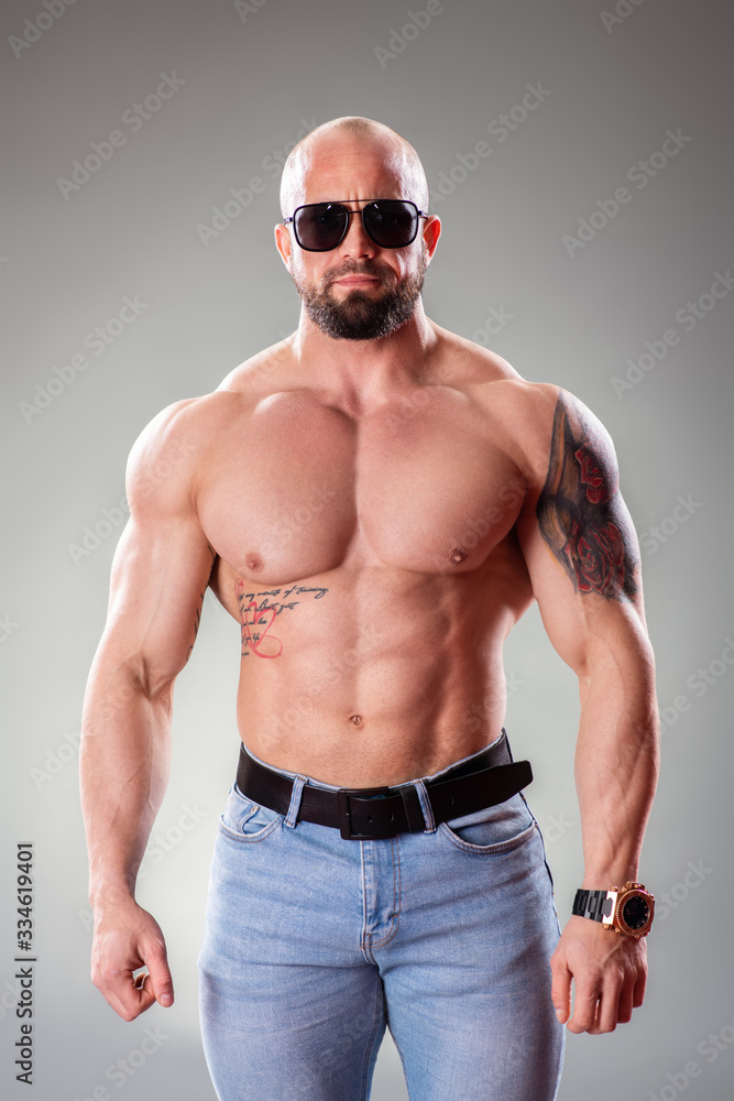 Sexy muscular bodybuider with sunglasses posing on the gray background