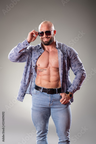 Sexy unbuttoned muscular bodybuider with sunglasses on the gray background photo