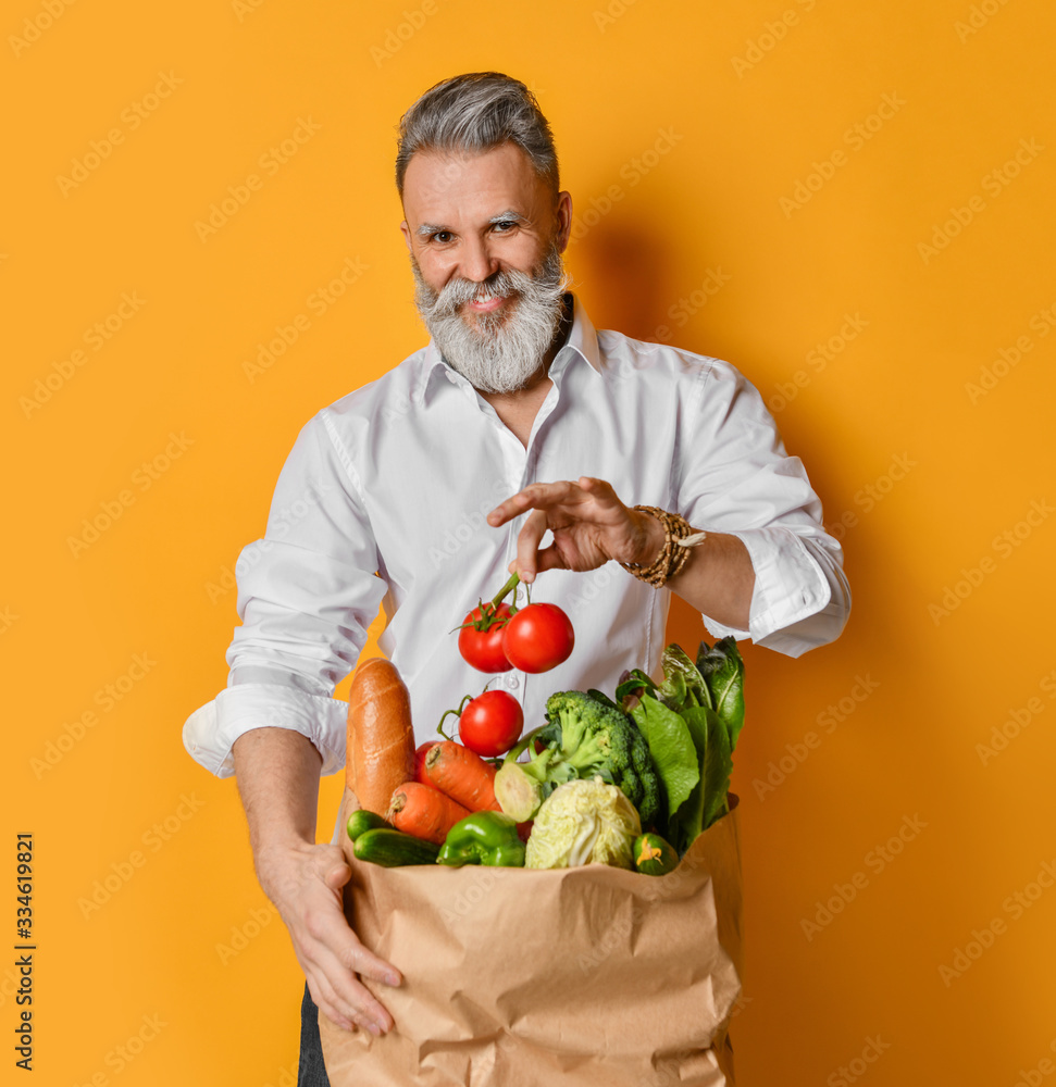 Cool old mature senior man with gray beard shopping hold grocery shopping bag with healthy organic vegetables on yellow Cool old mature senior man with gray beard shopping hold grocery shopping bag with healthy organic vegetables on yellow