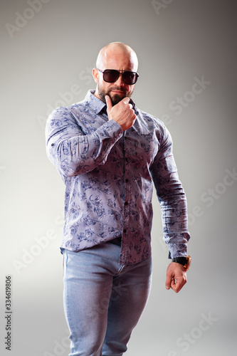 Sexy dressed muscular bodybuider with sunglasses on the gray background