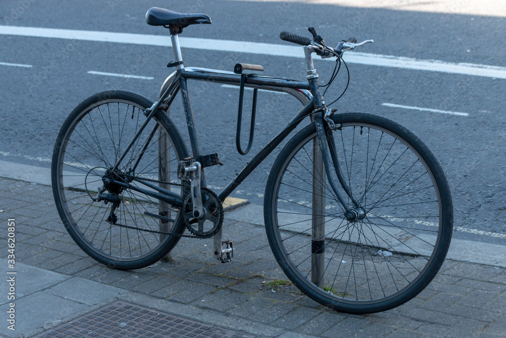 a close up view of a black bycycle locked onto a bike pole outside a shupermarket a close up view of a black bycycle locked onto a bike pole outside a shupermarket