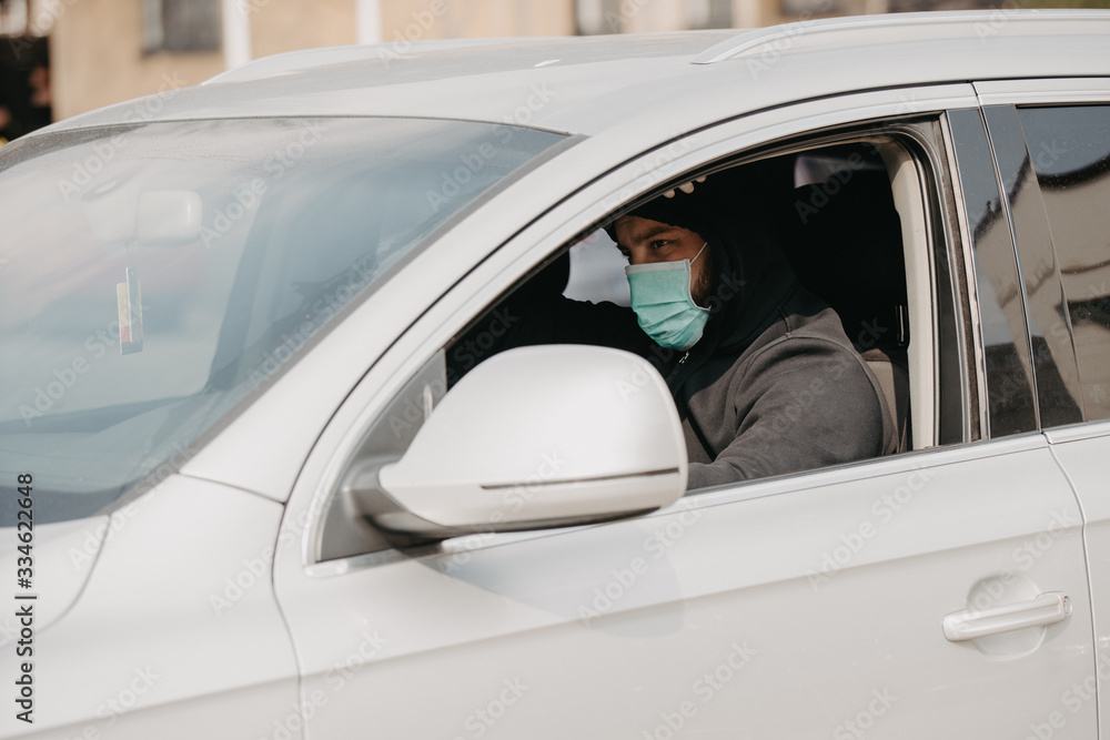 Pandemic outbreak. Man in the medical mask and rubber gloves for protect himself from bacteria and virus while driving a car.