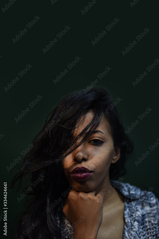 young African woman posing at studio, face with hand portrait over dark background	