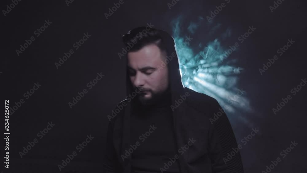 guy in a black hood sits on a bench looking at camera with glare guy in a black hood sits on a bench looking at camera with glare