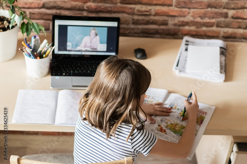 The concept of distance online learning self-isolation. Child sitting home desk doing lessons through a digital laptop.