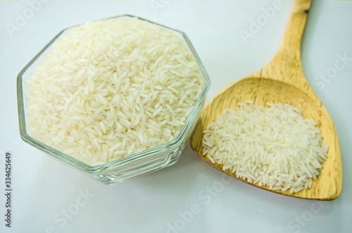 Milled rice in glass cup and wooden spoon for cooking