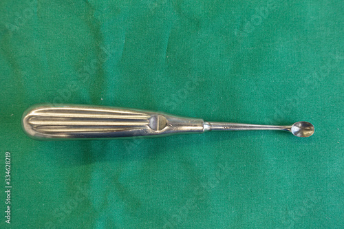 on  green surgical drape lies a sharp spoon for an operation photo