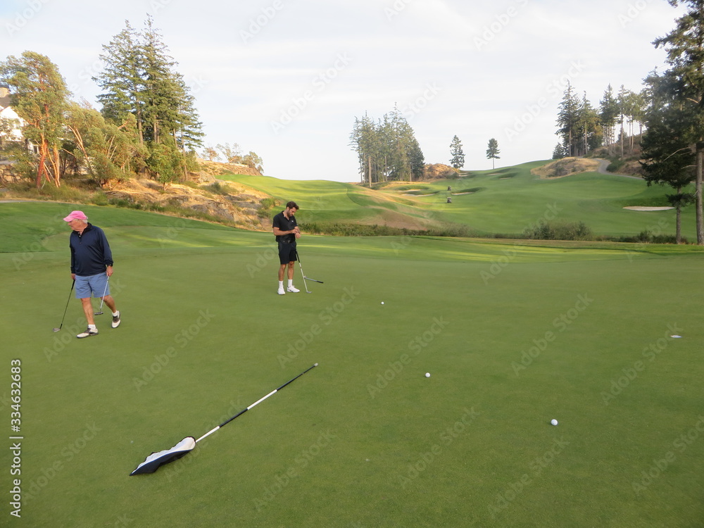 A father and son on a putting green playing golf surrounded by beautiful scenery outside of Victoria, British Columbia, Canada. A father and son on a putting green playing golf surrounded by beautiful scenery outside of Victoria, British Columbia, Canada.