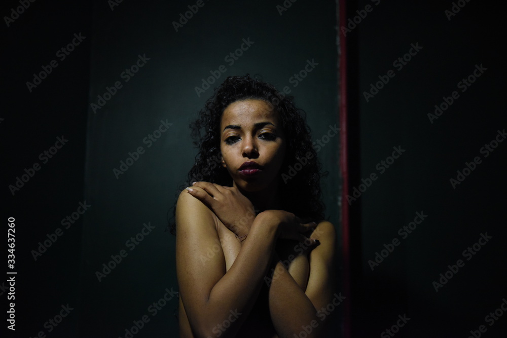 young naked African woman posing at studio, face with hand portrait over dark background	