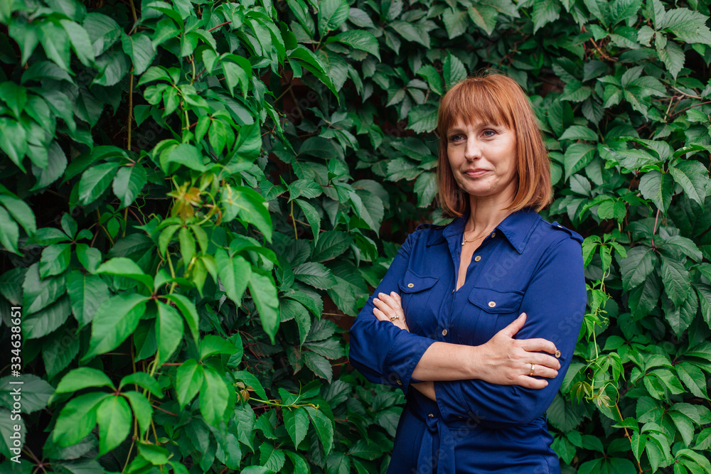 Portrait of a beautiful middle aged woman, standing next to the wall of wild grape leaves. Portrait of a beautiful middle aged woman, standing next to the wall of wild grape leaves.