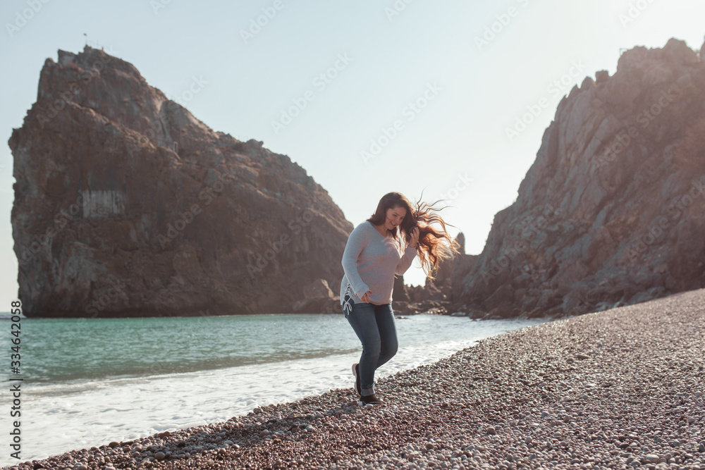 Happy pretty girl walks along the sea coast against the background of the sea and rocks, from behind a beautiful landscape