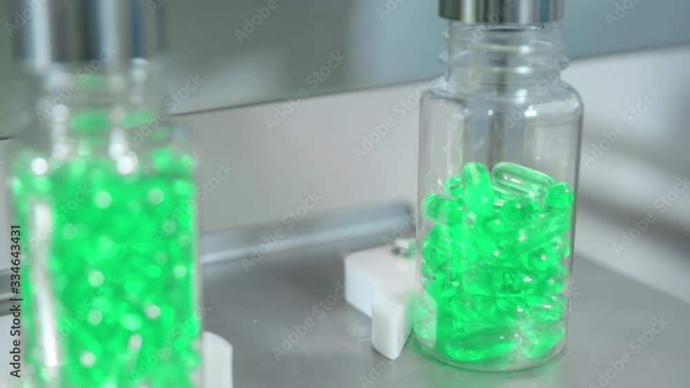 A pharmaceutical lab machine filling bottles with the green gel capsules A pharmaceutical lab machine filling bottles with the green gel capsules