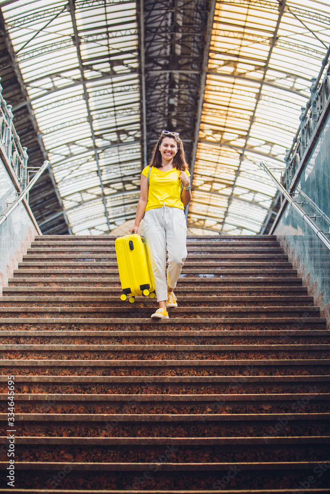 woman going down by stairs with yellow suitcase on wheels