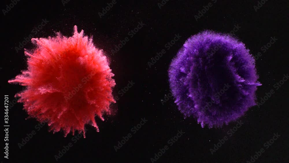 In real slow motion footage against a black background, a red pile and purple pile of powder explode burst in four directions like a firework. Top shot.