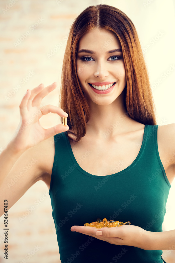 Portrait of smiling attractive woman with Omega 3 fish oil capsule, indoor. Health care and medical concept. Portrait of smiling attractive woman with Omega 3 fish oil capsule, indoor. Health care and medical concept.
